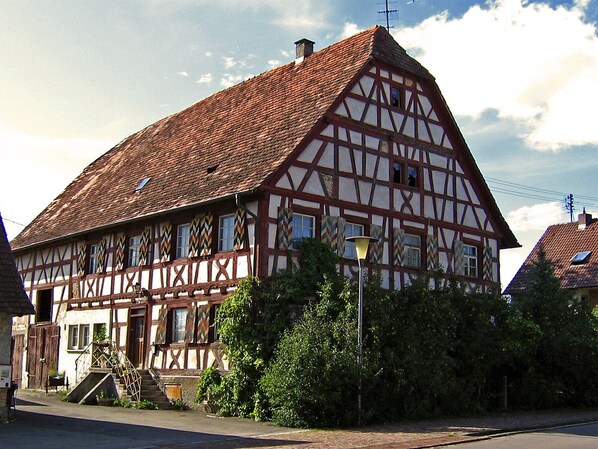 A traditional half-timbered house with a steeply pitched roof, a visible chimney, and a small porch with steps leading to the entrance.