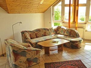 Un soggiorno con soffitto in legno, un divano floreale, un tavolino in legno e vista attraverso ampie finestre.