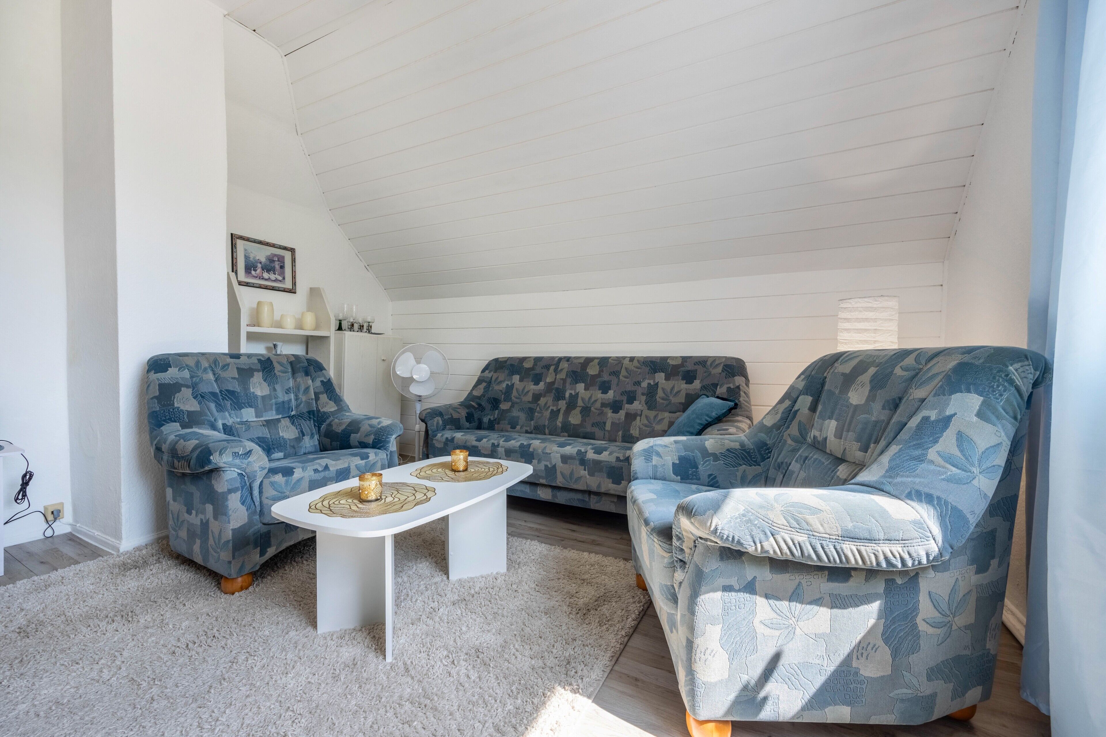 Ein Wohnzimmer mit zwei gemusterten Sofas, einem weißen Couchtisch und einem weißen Ventilator.