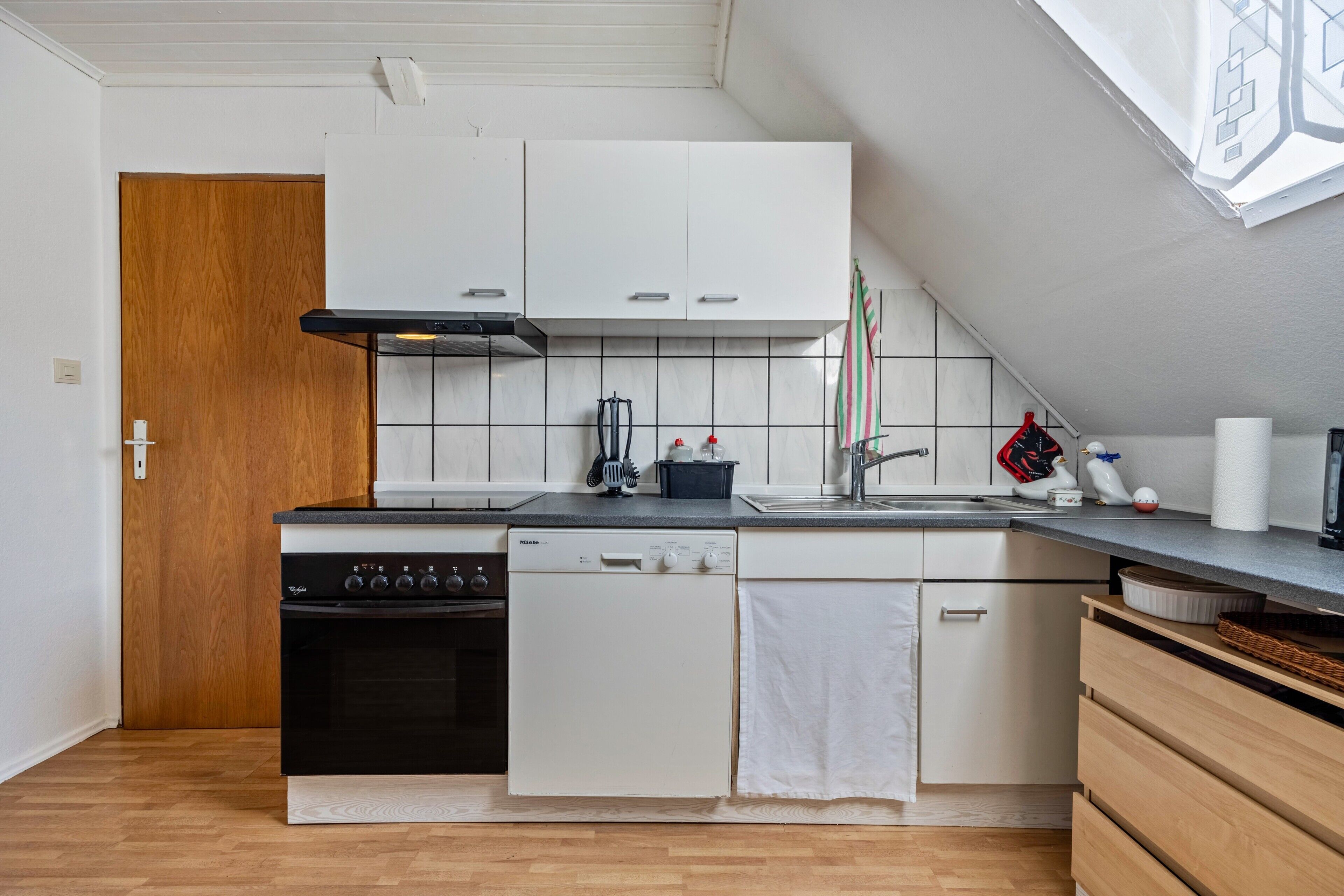 A compact kitchen with a stove, dishwasher, and white cabinets.