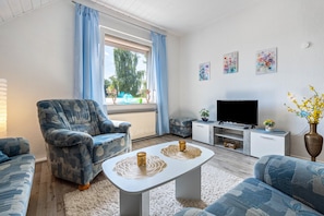 Un salon comprenant un canapé, un fauteuil, une table basse, un téléviseur et des œuvres d’art accrochées au mur.