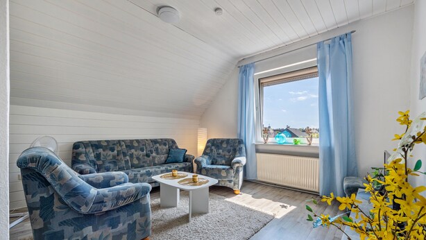 A cozy living room with a sofa, armchairs, a coffee table, and a view through a window.
