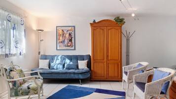Ein Wohnzimmer mit einem blauen Sofa, weißen Korbstühlen, einer Holzkommode und einem Gemälde an der Wand.