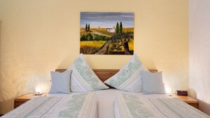 A bedroom with a bed, pillows, a nightstand, a painting, and a clock.