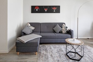 Een moderne woonkamer met een grijze bank, een ronde salontafel en een zeshoekige bijzettafel.