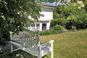 Een witte bank in een tuin met een wit gebouw op de achtergrond.