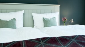 A hotel room with two beds, each with white linens and green pillows, a dark wall, and a small table with a vase of flowers.