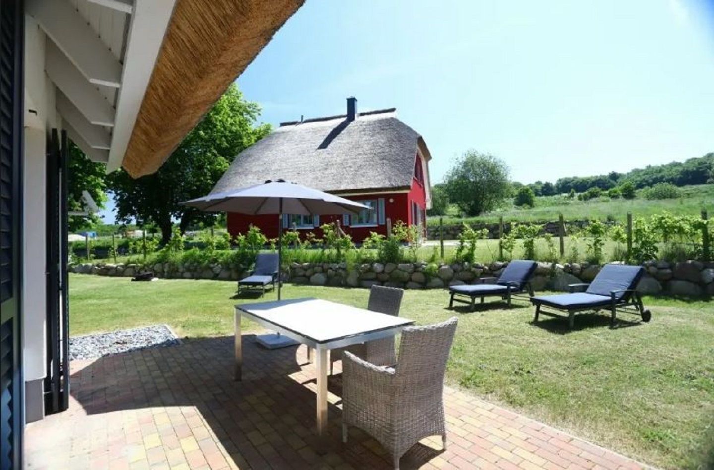 A patio with a table and chairs, a thatched roof, and a red house in the background.