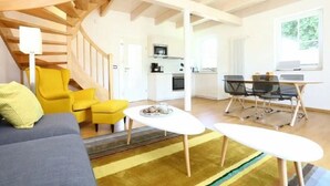 Een moderne woonkamer met een bank, gele stoelen, een eettafel en een keuken op de achtergrond.