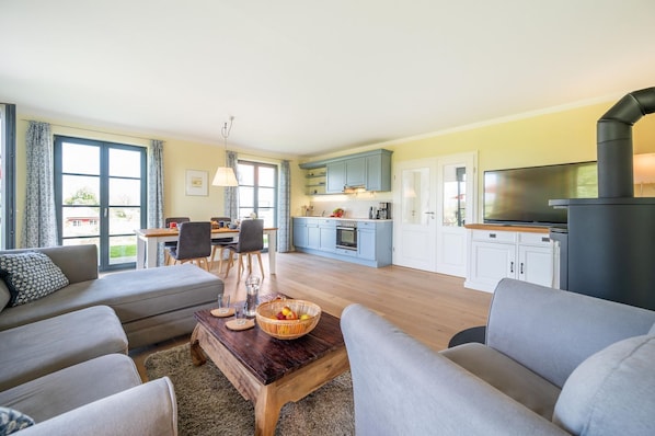 A modern living room with a sofa set, a coffee table with fruit, and a kitchen area with cabinets and a TV.