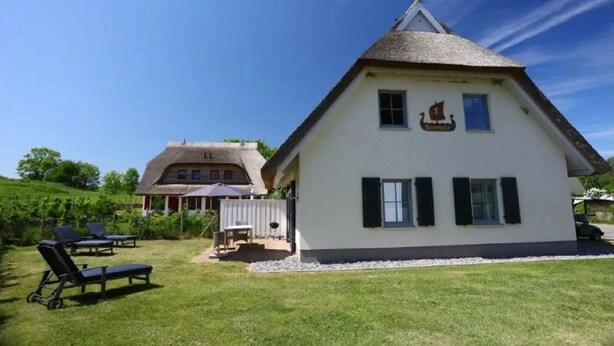 Een wit gebouw met een steil dak en een bord waarop een restaurant wordt aangegeven. Er zijn buiten zitplaatsen met tafels en stoelen.