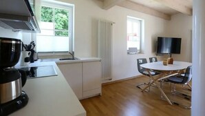 Een moderne keuken met witte kasten, een groot raam en een eethoek met een ronde tafel en stoelen.