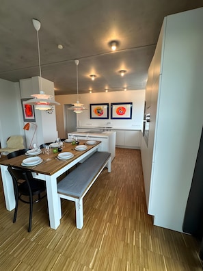 A modern kitchen with white cabinetry, a wooden dining table, and pendant lighting.