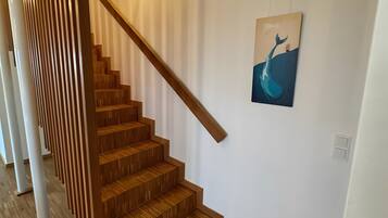 Un escalier avec des marches en bois et une rampe en bois, menant à un palier où se trouve un luminaire fixé au mur et un tableau représentant une baleine.