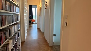A hallway with wooden flooring, white walls, and a bookshelf filled with books. - Holiday Home 'Großzügiges Modernes' with Shared Terrace, Private Garden and Wi-Fi (Neuharlingersiel)