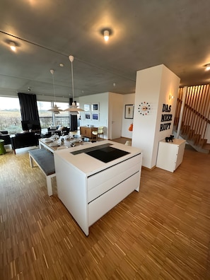 A modern kitchen with a central island, dining area, and large windows.