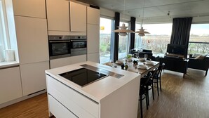 A modern kitchen with a central island, built-in oven, and a dining area with a view. - Holiday Home 'Großzügiges Modernes' with Shared Terrace, Private Garden and Wi-Fi (Neuharlingersiel)
