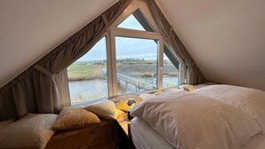 A bedroom with a sloped ceiling, large windows, a wooden desk, and a bed with white bedding. - Holiday Home 'Großzügiges Modernes' with Shared Terrace, Private Garden and Wi-Fi (Neuharlingersiel)