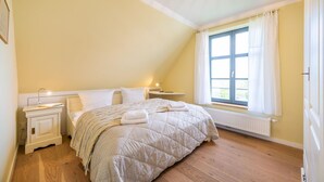 Ein Schlafzimmer mit Bett, Nachttischen, einem Fenster mit Vorhängen und einer Heizung.