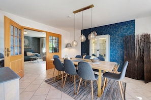 A modern dining area with a wooden table, grey chairs, hanging pendant lights, and a blue textured wall.