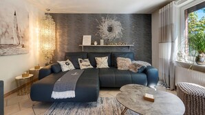 A modern living room with a sectional sofa, a round coffee table, a chandelier, and a view of the outdoors. - Holiday Home 'Ankerglück' with Private Terrace and Wi-Fi (Lensahn)