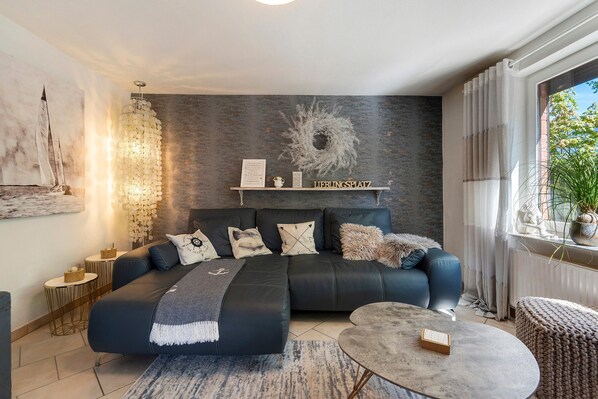 A modern living room with a sectional sofa, a round coffee table, a chandelier, and a view of the outdoors.