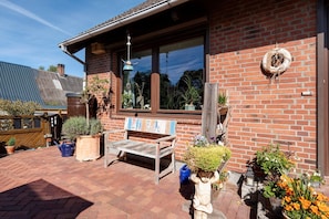 A brick building with a wooden bench, potted plants, and a wreath on the wall.