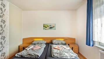 A double bed with two pillows, a bedside table, a small drawer, and a wall-mounted picture.