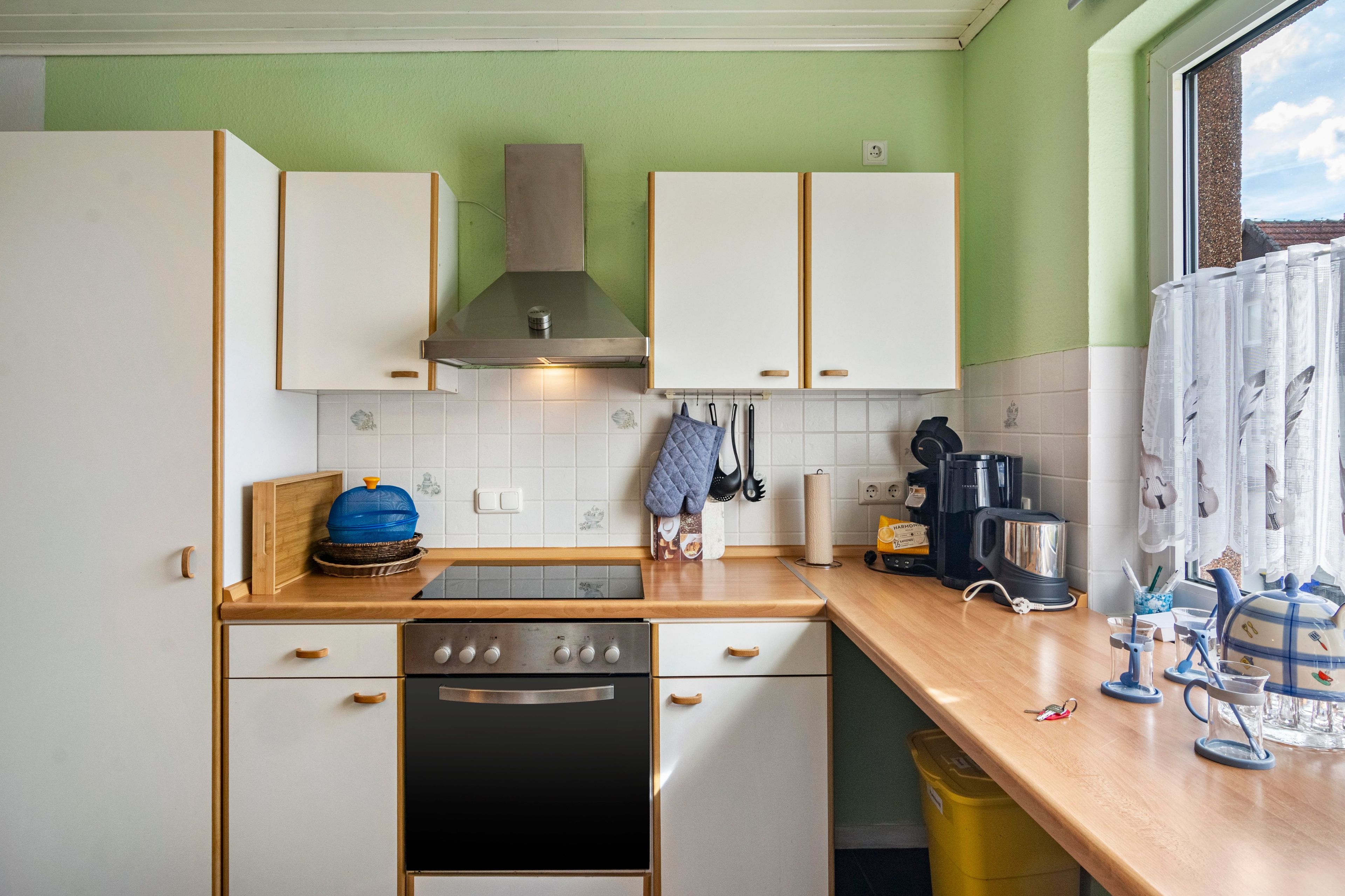 Een keuken met witte kasten, een roestvrijstalen afzuigkap, een vaatwasser en een koffiezetapparaat.