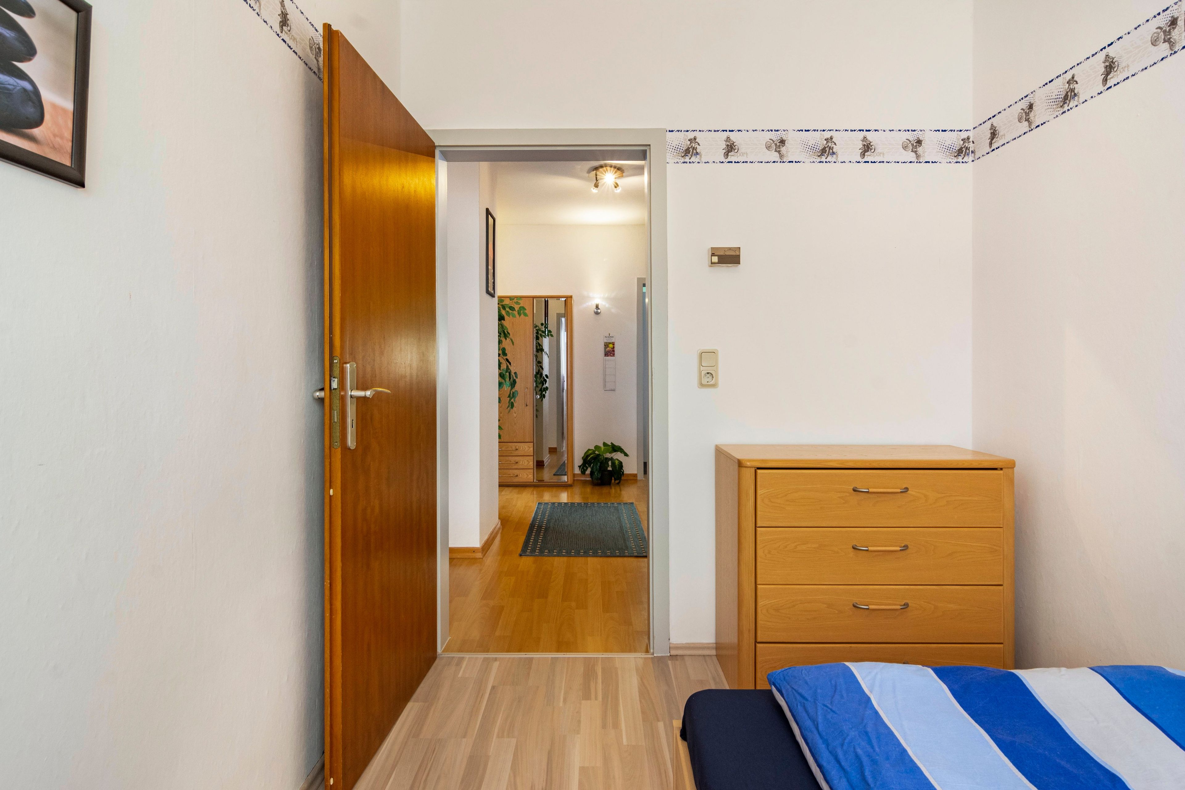 Une chambre à coucher avec un lit, une commode en bois et une porte donnant sur un couloir.