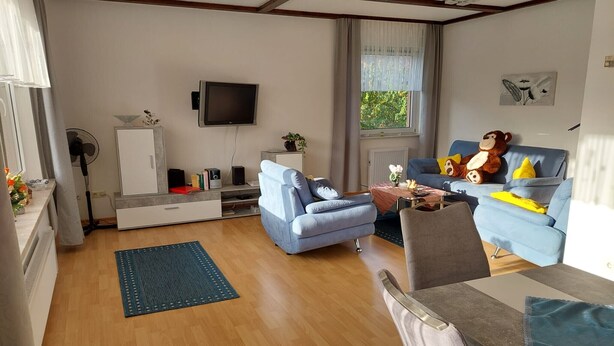 A living room with a flat-screen TV, a blue sofa, a coffee table, and a teddy bear. - Apartment 'Wolfswind' with Mountain View, Balcony and Wi-Fi (Langelsheim)