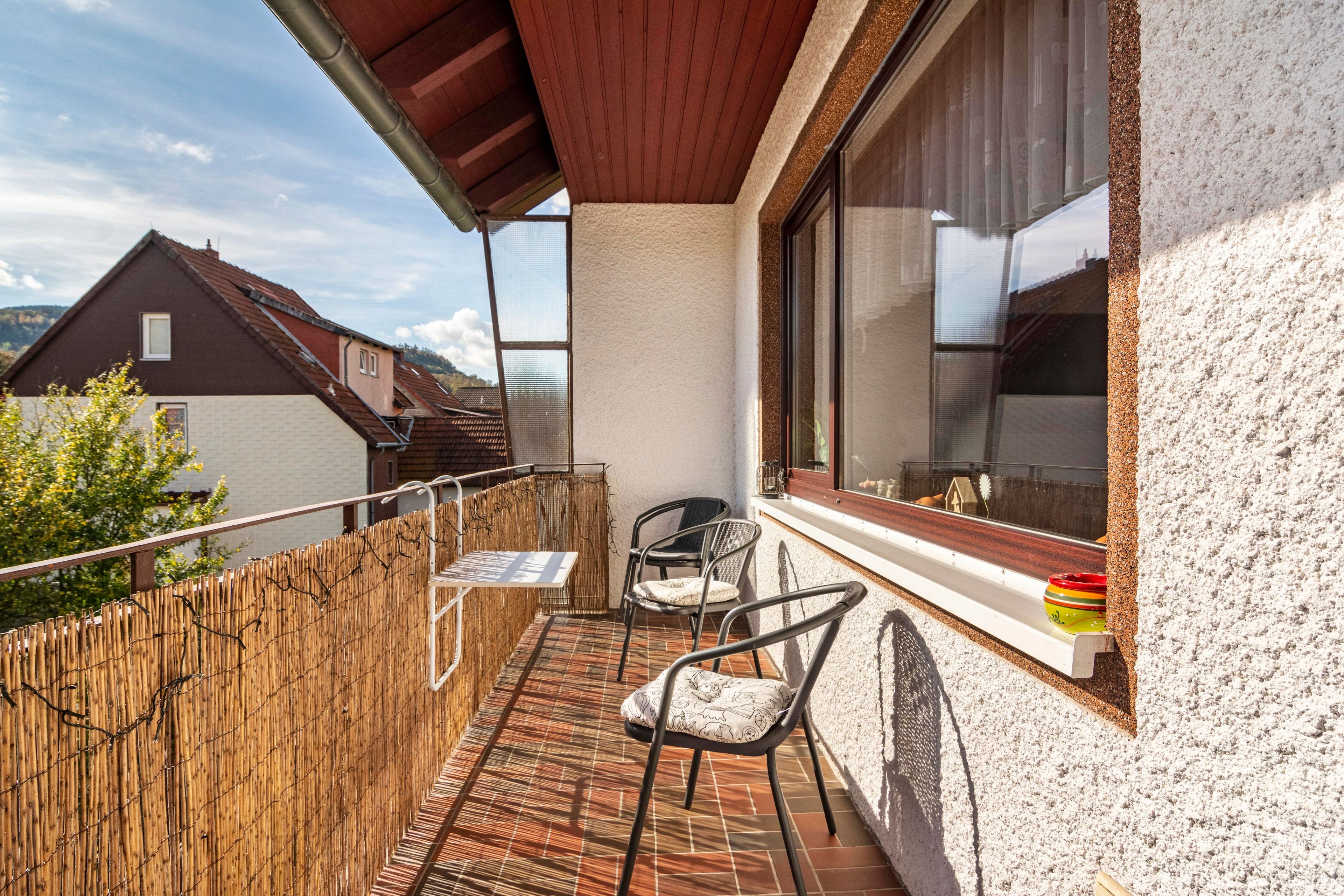 Ein Balkon mit Tisch und Stühlen, einem Holzzaun und Blick auf benachbarte Häuser.