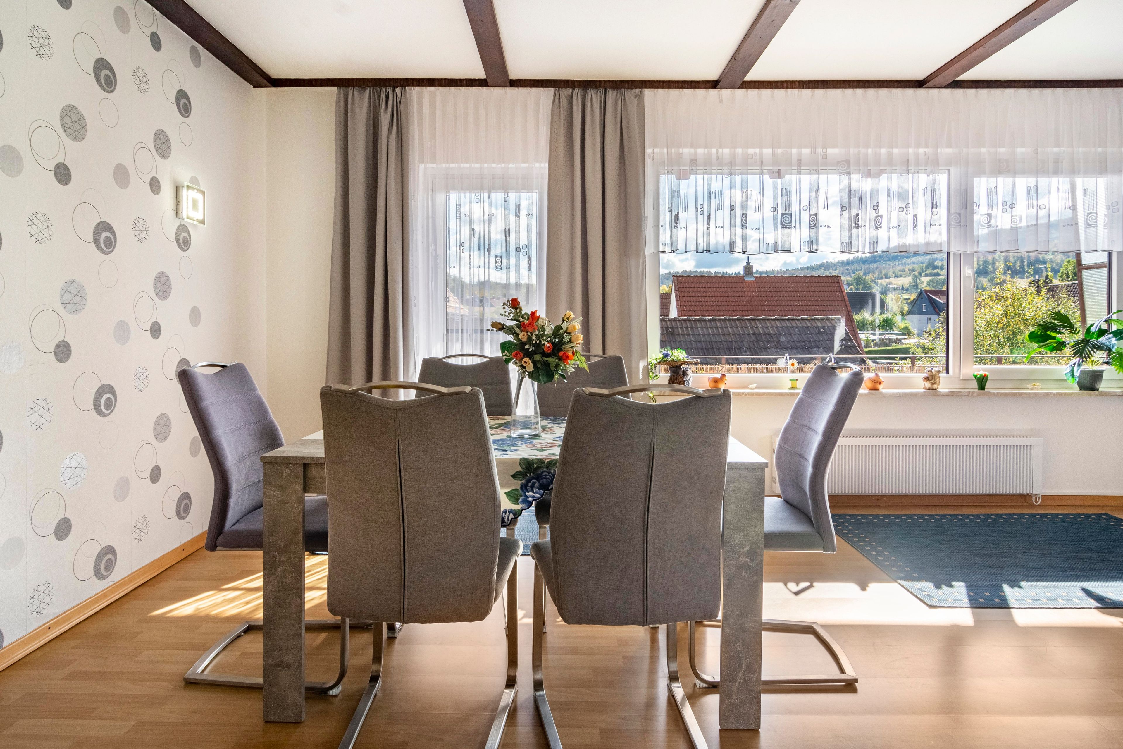 A dining area with a table, chairs, and a view of a rural landscape through large windows.