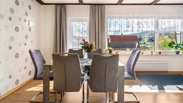 A dining area with a table, chairs, and a view of a rural landscape through large windows.