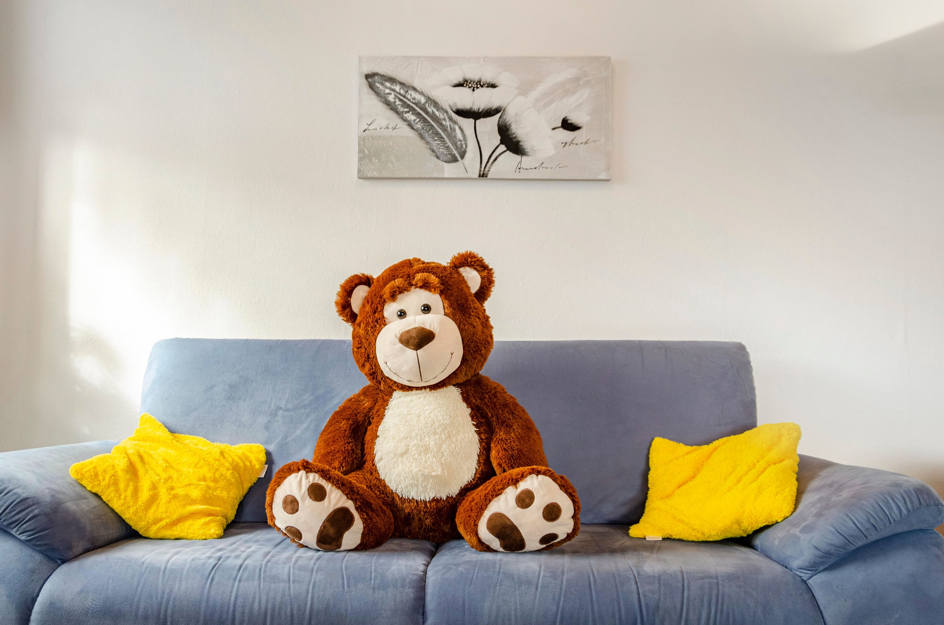 Ein Plüschbär auf einem blauen Sofa mit zwei gelben Kissen.