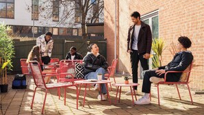 Een terras met rode metalen stoelen en tafels, omringd door bakstenen muren en potplanten.