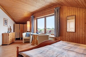 Een slaapkamer met een houten plafond, een bed, een bureau, een stoel en een raam met gordijnen.