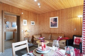 A wooden-paneled room with a sofa, a dining table with a red and white checkered tablecloth, and a framed picture on the wall. - Apartment 'Morgensonne' with Mountain View, Private Terrace and Wi-Fi (Höchenschwand)