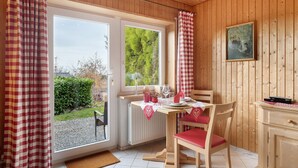 Ett rum med träpanel på väggarna, ett bord dukat för två personer, ett element och ett fönster med utsikt över grönområden.