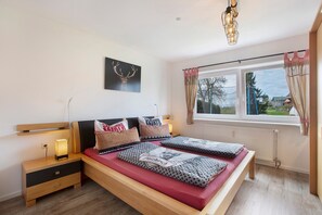 Un dormitorio con cama, mesitas de noche, una ventana con cortinas, un radiador y una obra de arte en la pared.