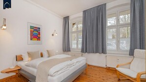 Une chambre moderne avec un grand lit, une chaise, un radiateur et une fenêtre avec des rideaux.