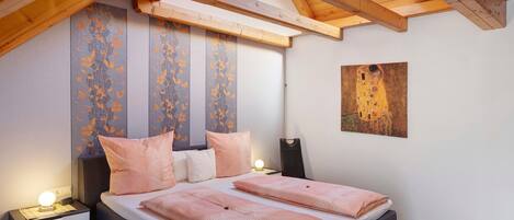 A bedroom with a bed, bedside tables, a nightstand, a ceiling with wooden beams, and a painting on the wall.