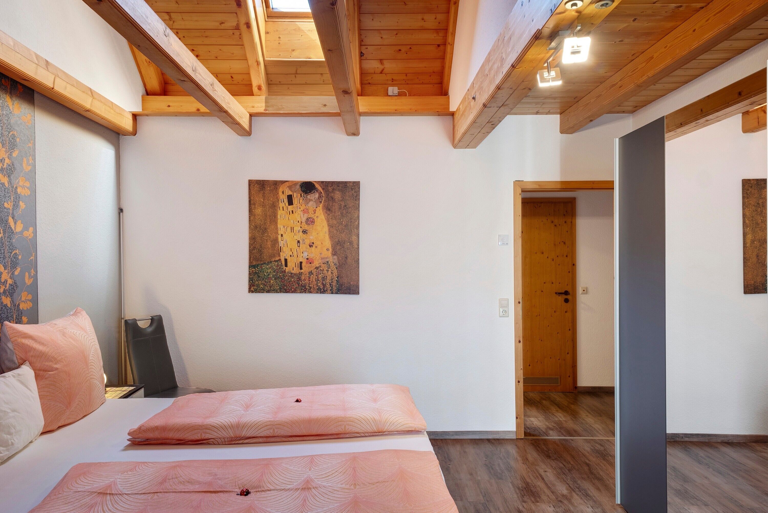 Ein Schlafzimmer mit einem Bett, einem Gemälde, Holzbalken und einer Tür.