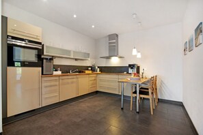 A modern kitchen with a dining area, featuring a built-in oven, microwave, and stainless steel range hood.