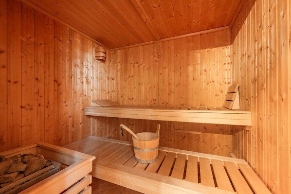 A wooden sauna with benches, a bucket, and a shelf.