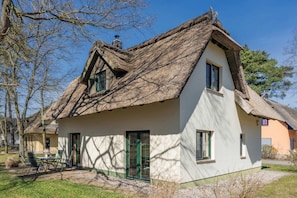 A traditional house with a thatched roof, a green door, and a small patio with outdoor furniture.