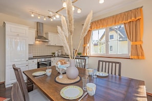 A dining area with a wooden table, chairs, a vase with pampas grass, and a window with curtains. - Vacation home "Ferien am Haff" - Detached vacation home with sauna & fireplace, quiet (Zirchow)