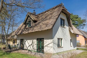 A traditional house with a thatched roof, a green door, and a small patio with outdoor furniture.