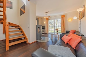 A modern living room with a wooden staircase, a fireplace, a sofa, and a dining area.