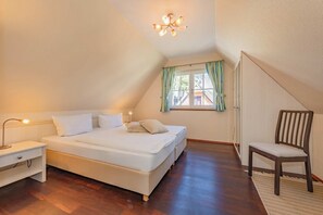 A bedroom with a bed, bedside table, lamp, chair, window with curtains, and a ceiling light fixture.